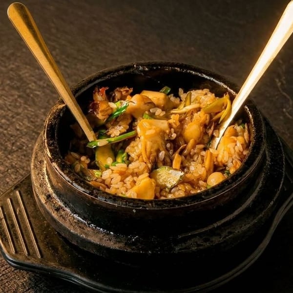 A stone bowl filled with rice, mushrooms, and vegetables, with two golden spoons.